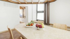 A dining area with a marble table, two white bowls with fruits and vegetables, wooden chairs, and a view of the kitchen through an open door. - Captivating Loft in Prime Location near Colosseum (Roma)