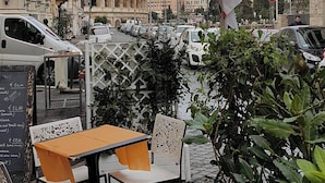 A street view with a cafe, outdoor seating, a columned building, and parked cars. - Captivating Loft in Prime Location near Colosseum (Roma)