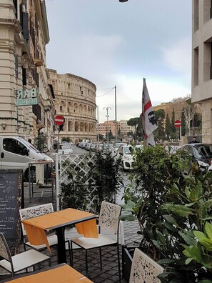 A street view with a cafe, outdoor seating, a columned building, and parked cars. - Captivating Loft in Prime Location near Colosseum (Roma)