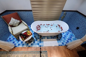 A bathroom with a bathtub, a chair with a cushion, a tray with fruits, and a decorative rug. -  Hai Bot Home A100 (Phu Quoc)