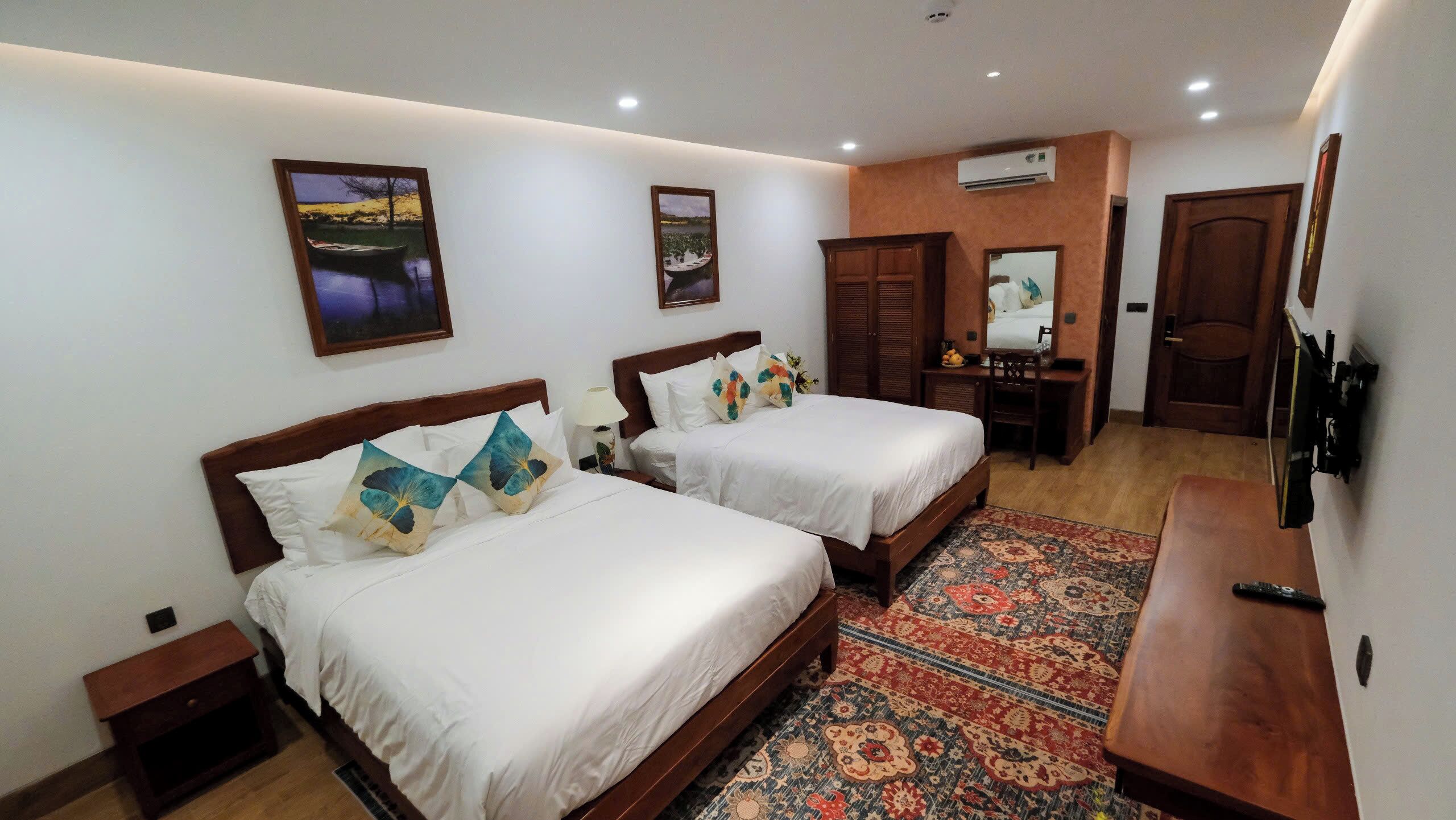 A hotel room with two beds, a desk, a chair, a TV, and a patterned rug.