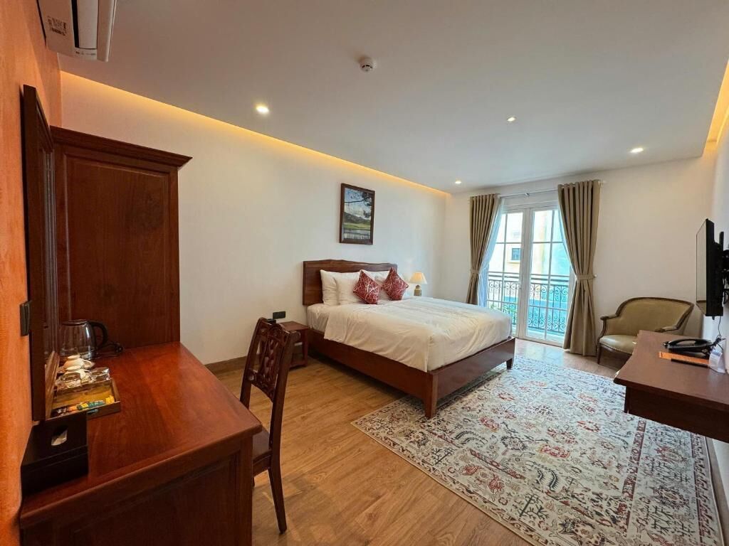 A hotel room with a bed, a desk, a chair, a coffee machine, and a window with curtains.