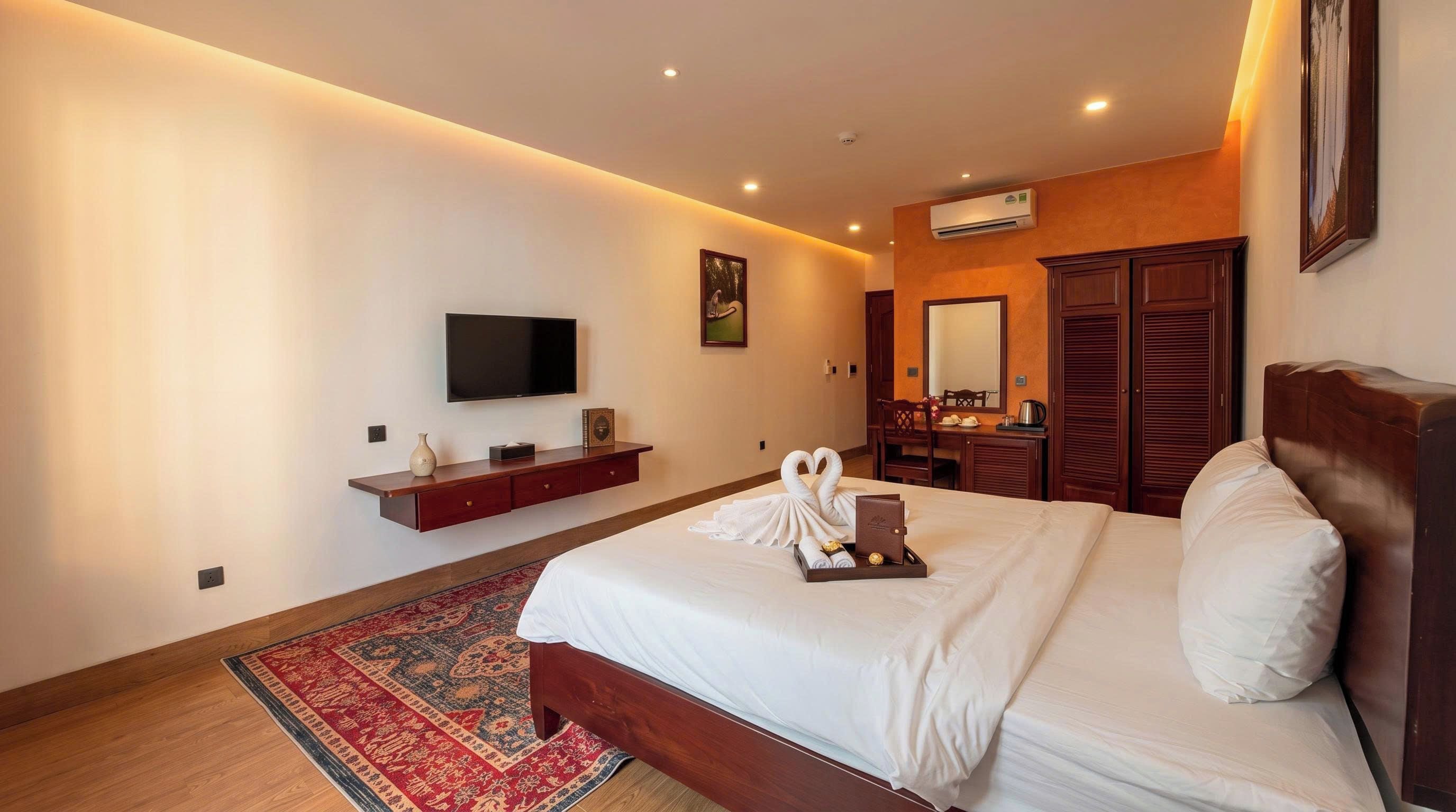 Una habitación de hotel con una cama, un televisor de pantalla plana, un aparador de madera, un espejo y un tapete rojo estampado.