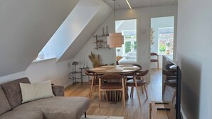 A modern living room with a sectional sofa, a dining table with chairs, a TV, and a ceiling light. - Bright modern holiday apartment on Samsø (Samsø)