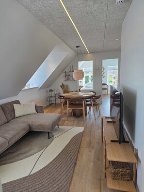 A modern living room with a sectional sofa, a dining table with chairs, a TV, and a ceiling light.