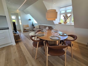 A modern dining area with a round table set for six, wooden flooring, and a large window with a view.