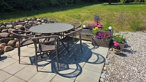 An outdoor patio with a round table and wicker chairs, surrounded by a stone wall and potted plants. - Bright modern holiday apartment on Samsø (Samsø)