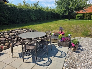 An outdoor patio with a round table and wicker chairs, surrounded by a stone wall and potted plants.