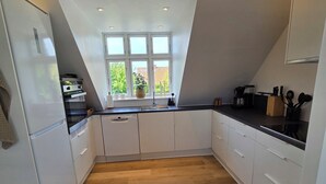 A modern kitchen with white cabinetry, a wooden herringbone floor, a window with a view, and a built-in oven. - Bright modern holiday apartment on Samsø (Samsø)