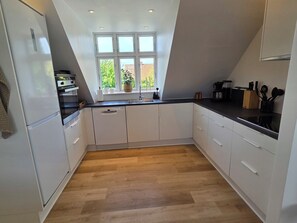 A modern kitchen with white cabinetry, a wooden herringbone floor, a window with a view, and a built-in oven.