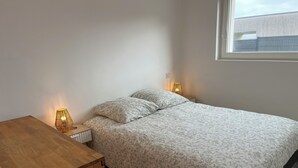 Een slaapkamer met een bed, twee bedlampen, een houten nachtkastje en een raam.