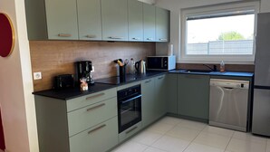 Een moderne keuken met lichtgroene kastjes, een zwart aanrecht, een koffiezetapparaat, een magnetron, een vaatwasser en een raam met uitzicht.