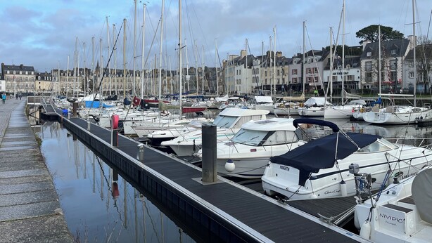 Een jachthaven met aan wal liggende boten, een houten looppad en gebouwen op de achtergrond.