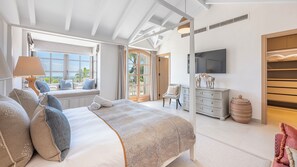 Ein Schlafzimmer mit einem großen Bett, einem Fernseher, einem Sessel und einem Fenster mit Aussicht.