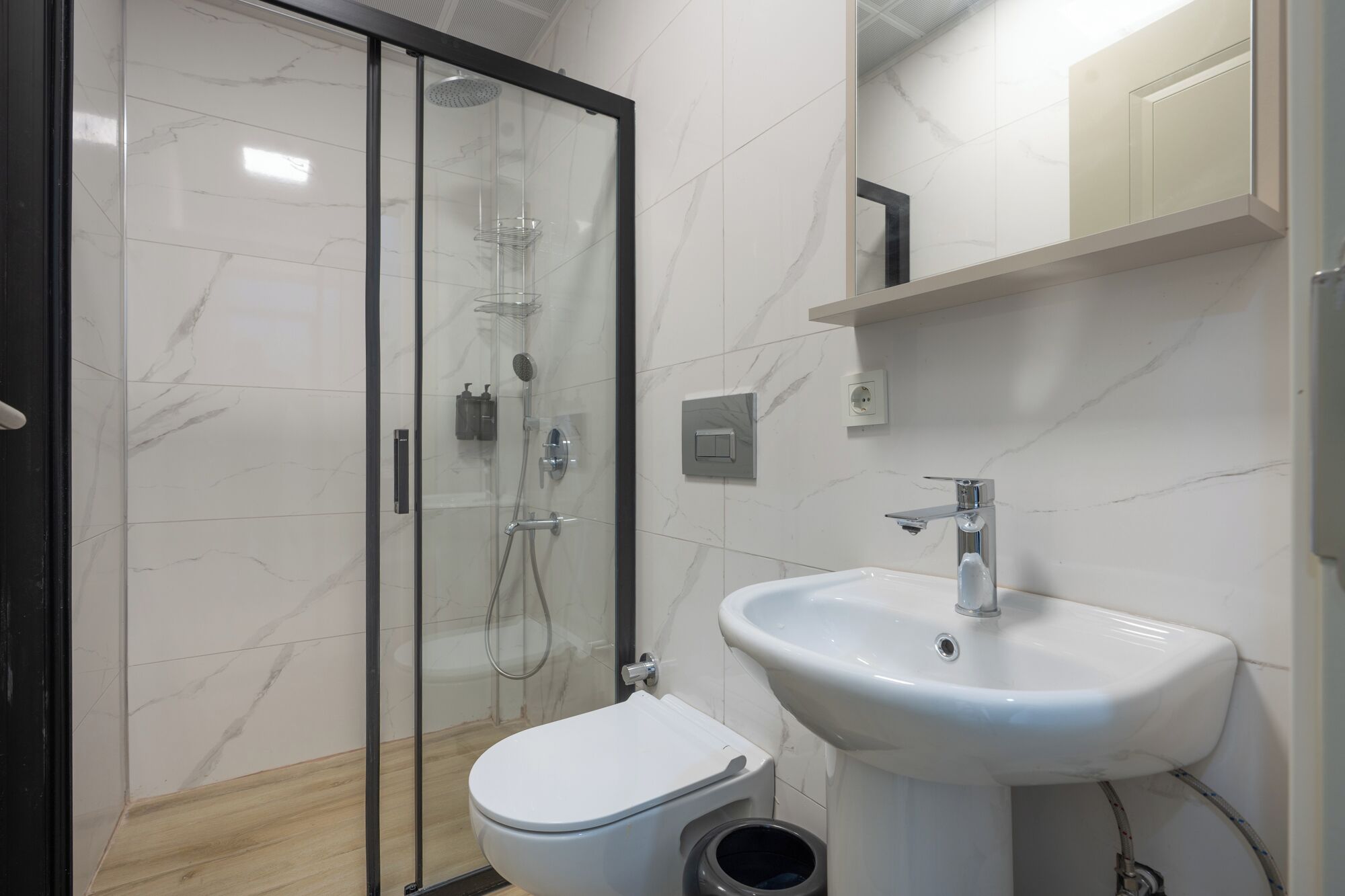 Un bagno moderno con doccia vetrata, un water bianco e un lavabo su piedistallo.
