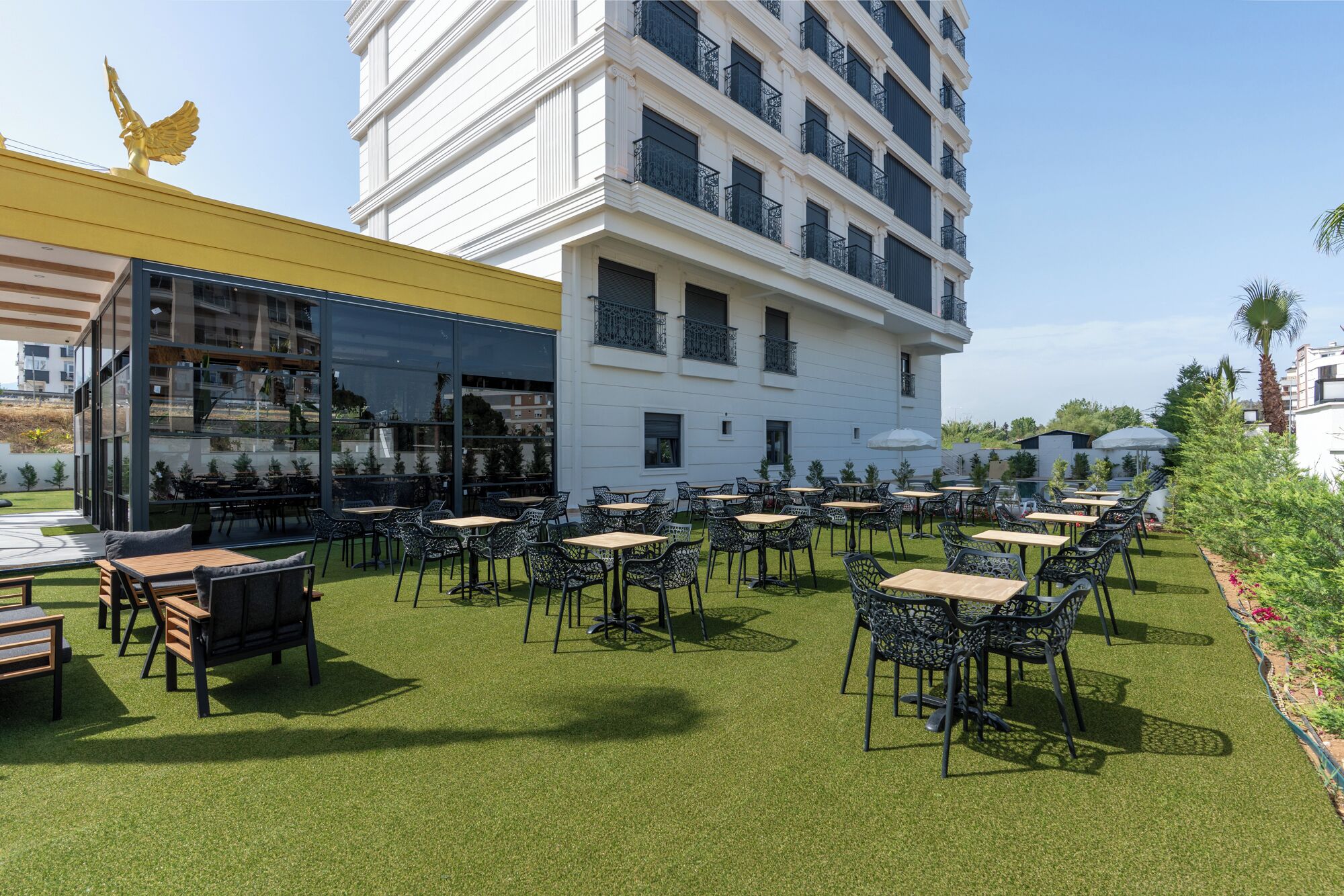 Een terras met tafels en stoelen, een gebouw met balkons, en een gouden standbeeld van een Amerikaanse adelaar.