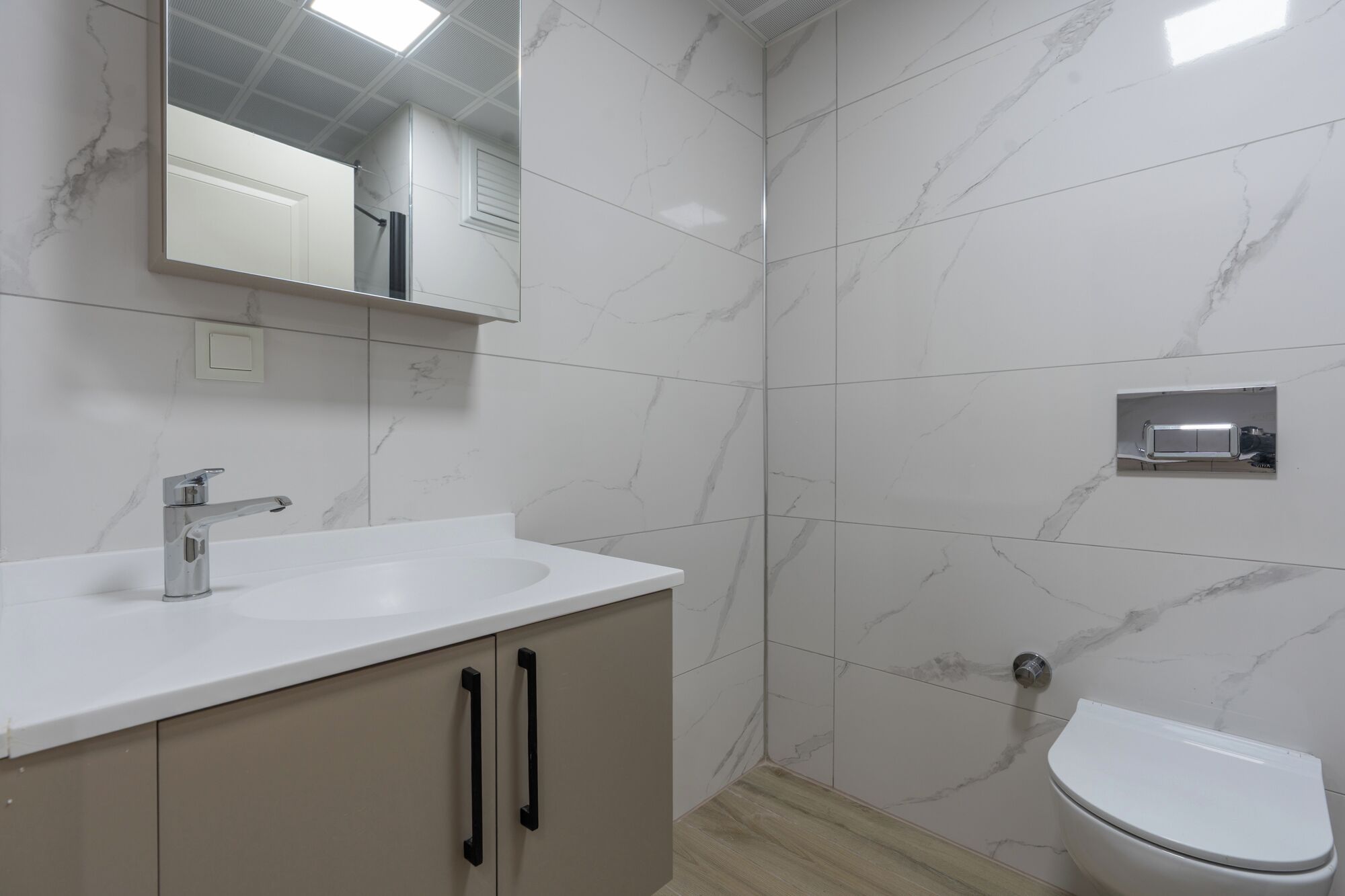 Een badkamer met een witte wastafel, een spiegel, een toilet en een douche.