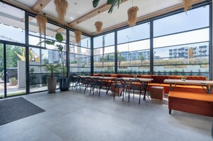 Un interior moderno con grandes ventanales, una zona de estar con sofás naranjas y plantas colgantes.