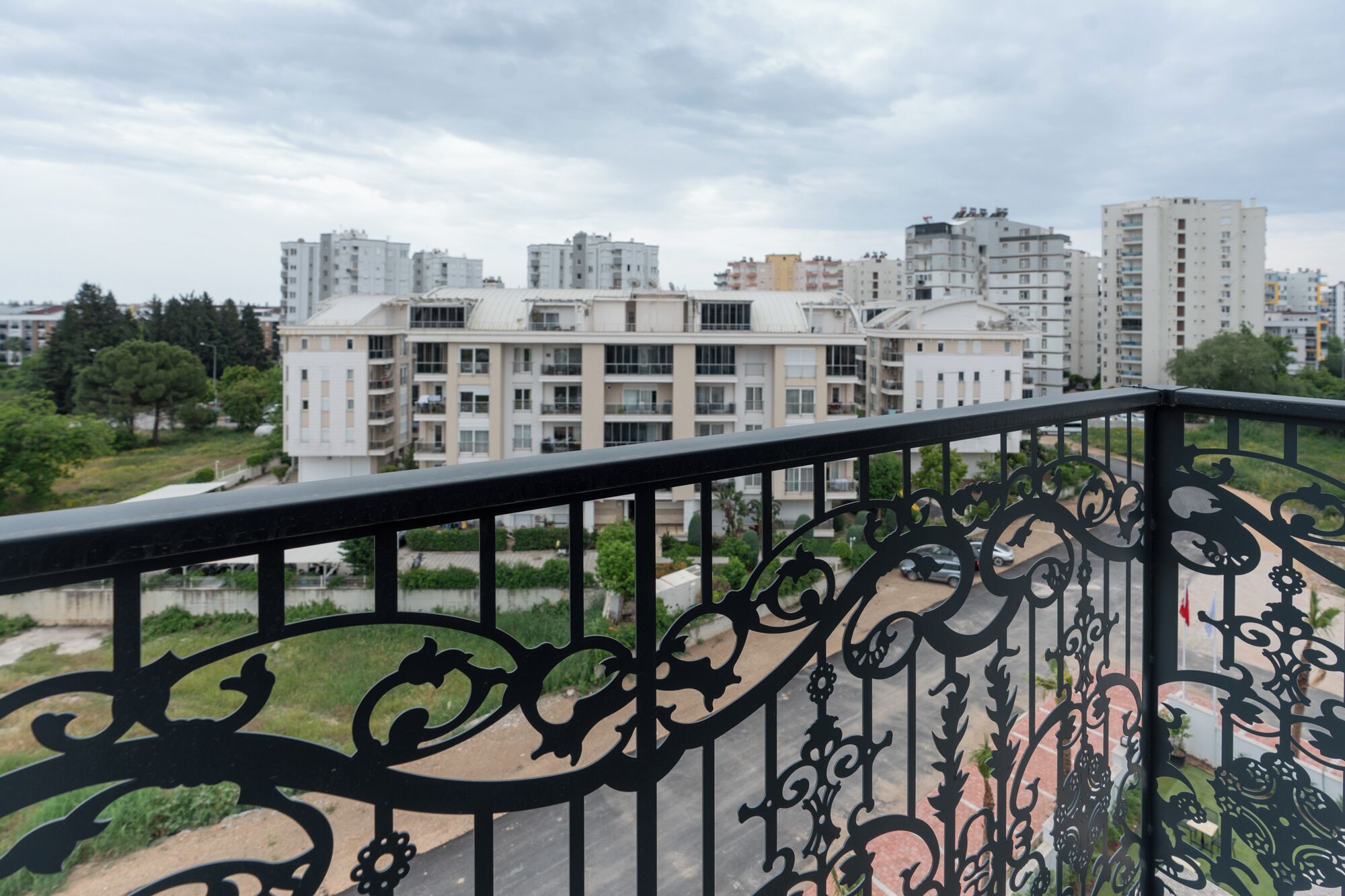 Un balcó amb barana de metall negre decorativa que domina una zona residencial amb edificis d'altes plantes.