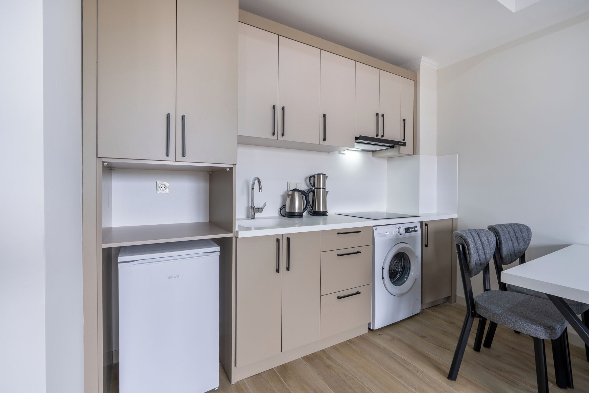 A compact kitchen with a washing machine, a coffee maker, and a small refrigerator.