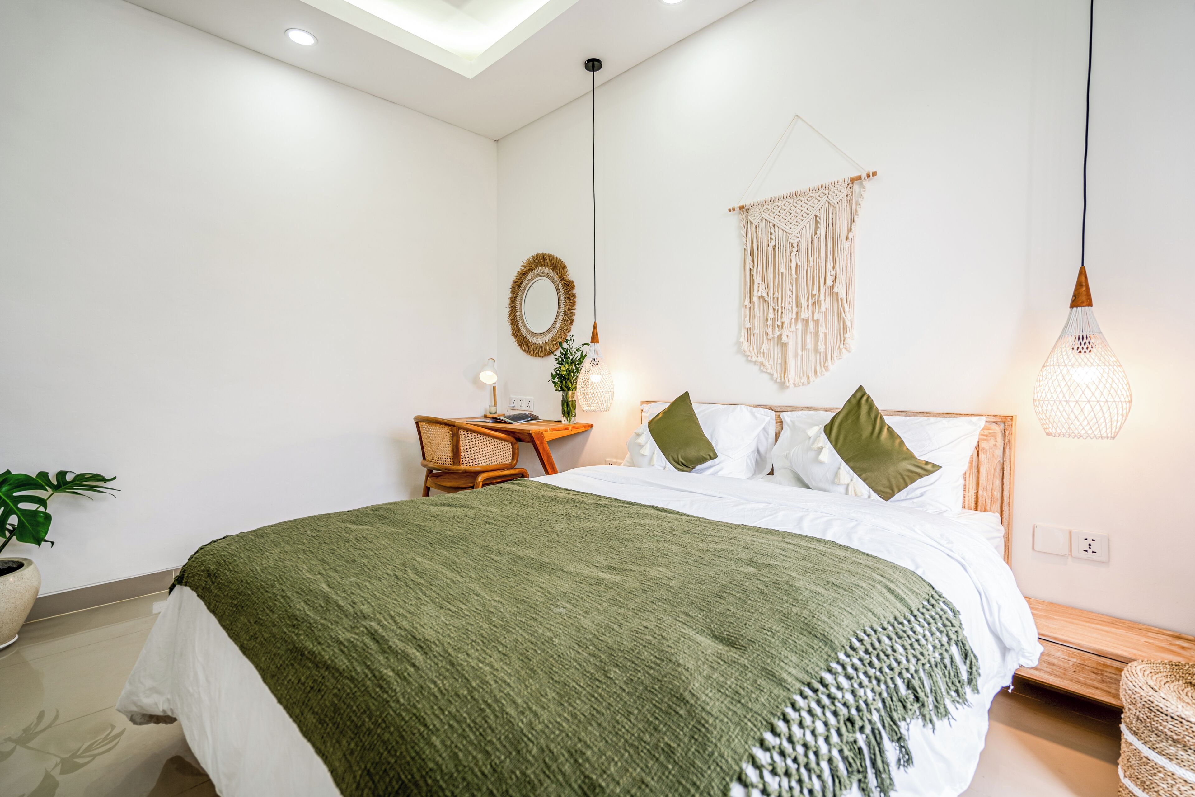Une chambre à coucher moderne avec un lit, une table de chevet, une lampe, une décoration murale en macramé et une plante en pot.