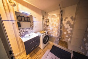Un bany petit i funcional amb rentadora, un lavabo i zona de dutxa.