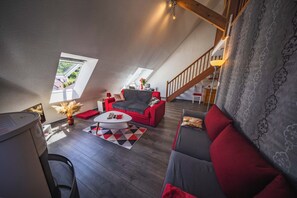 A loft-style living room with a red sofa, grey couch, and a white coffee table. There are two windows with a view of the outside, a staircase, and a lamp. - Vielle-aure Le 2 Bers duplex (90 M2)cosy mountain living ☀️ (Vielle-Aure)
