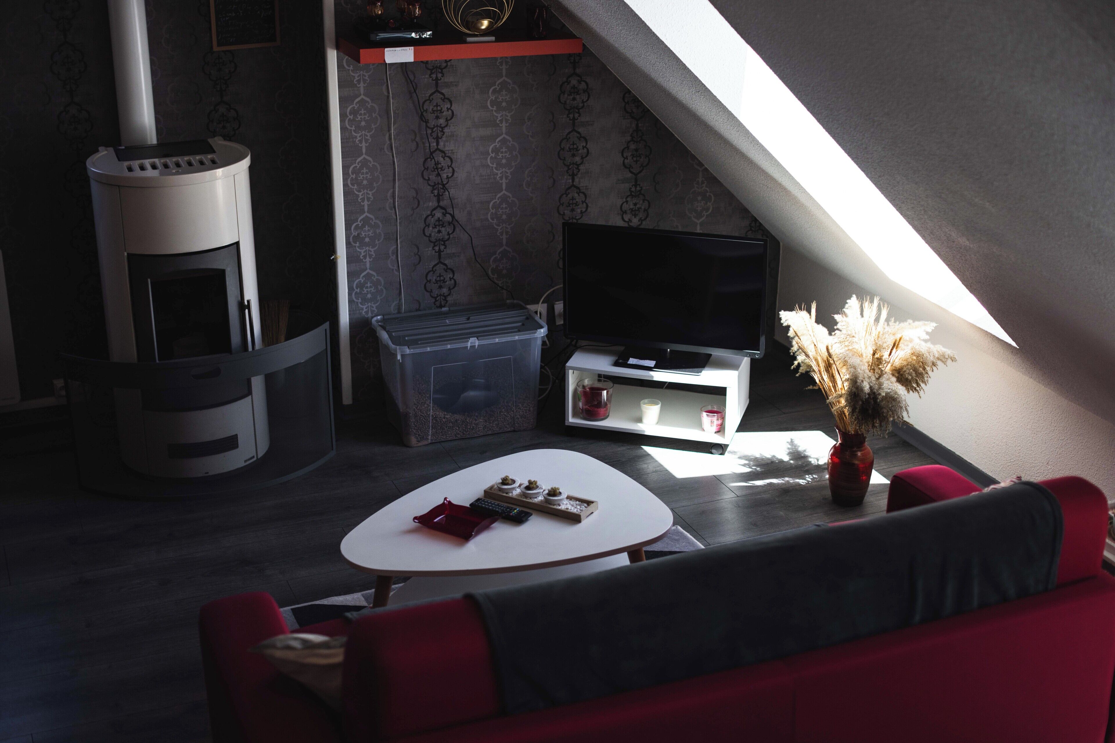 A cozy living area with a fireplace, a flat-screen TV, a small table, and a red sofa.
