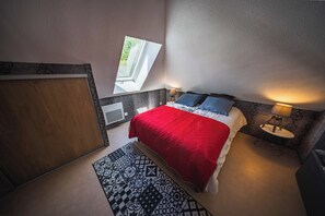 Een slaapkamer met een bed, een nachtkastje, een lamp, een raam en een kamerkleed met een patroon.