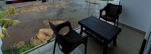 Un balcón con vista a una playa rocosa, dos sillas negras y una mesa pequeña.