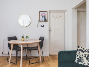 Ein Zimmer mit einem runden Tisch, zwei Stühlen, einem grünen Sofa, einer weißen Tür und einem gerahmten Bild an der Wand.