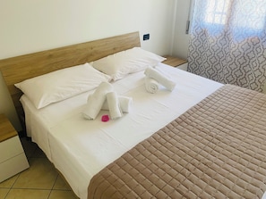 Una cama bien hecha con sábanas blancas, un edredón acolchado marrón y toallas enrolladas sobre la cama.