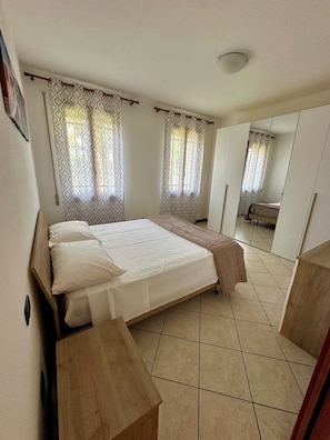 Un dormitorio con cama, mesita de noche de madera, armario y espejo.