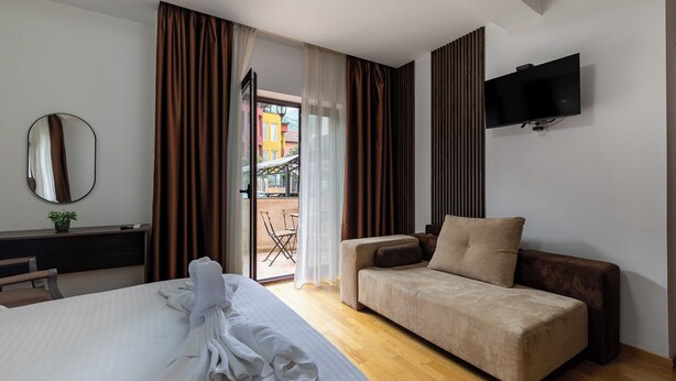 A hotel room with a bed, a sofa, a TV, a desk with a plant, and a view through a door. - Hillside Garden by Sienna (Skopje)