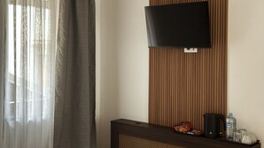 A room with a TV mounted on a wooden panel wall, a dark wooden console table with a kettle, a water bottle, and snacks. - Hillside Garden by Sienna (Skopje)