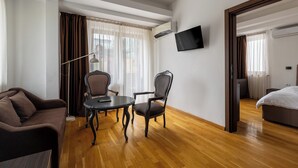 A hotel room with a wooden floor, a sofa, a dining table with chairs, a TV mounted on the wall, and a bed. - Hillside Garden by Sienna (Skopje)