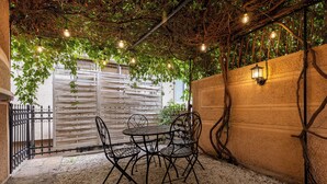 An outdoor seating area with a table and chairs, a pergola with hanging lights, and a wall-mounted lantern. - Hillside Garden by Sienna (Skopje)