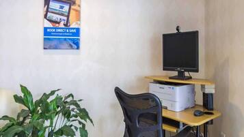 Ein Schreibtisch mit Computermonitor, Drucker und Tastatur. Vor dem Schreibtisch steht ein Stuhl. Eine Topfpflanze ist auf der linken Seite zu sehen.