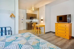 Una habitación compacta con cama, escritorio, silla, cómoda, televisor y kitchenette.