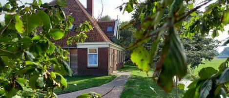 Een huis van baksteen met schuin dak, een zichtbaar raam en een pad naar de ingang.