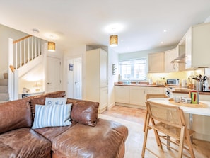 A modern interior with a leather sofa, wooden dining table, and a kitchen area. - Beautiful two bedroom seaside holiday cottage in Camber Sands. (Camber)