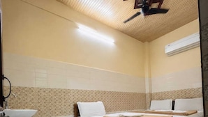 A room with a wooden ceiling, a bed with white bedding, a small bedside table, and a wall-mounted air conditioner. - Hotel Jannat Palace Near Jama Masjid (New Delhi)