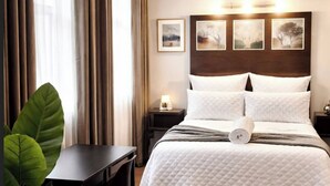 Ein Hotelzimmer mit einem Bett, einem Schreibtisch, einem Stuhl, einer Zimmerpflanze und einem Nachttisch mit einer Lampe.