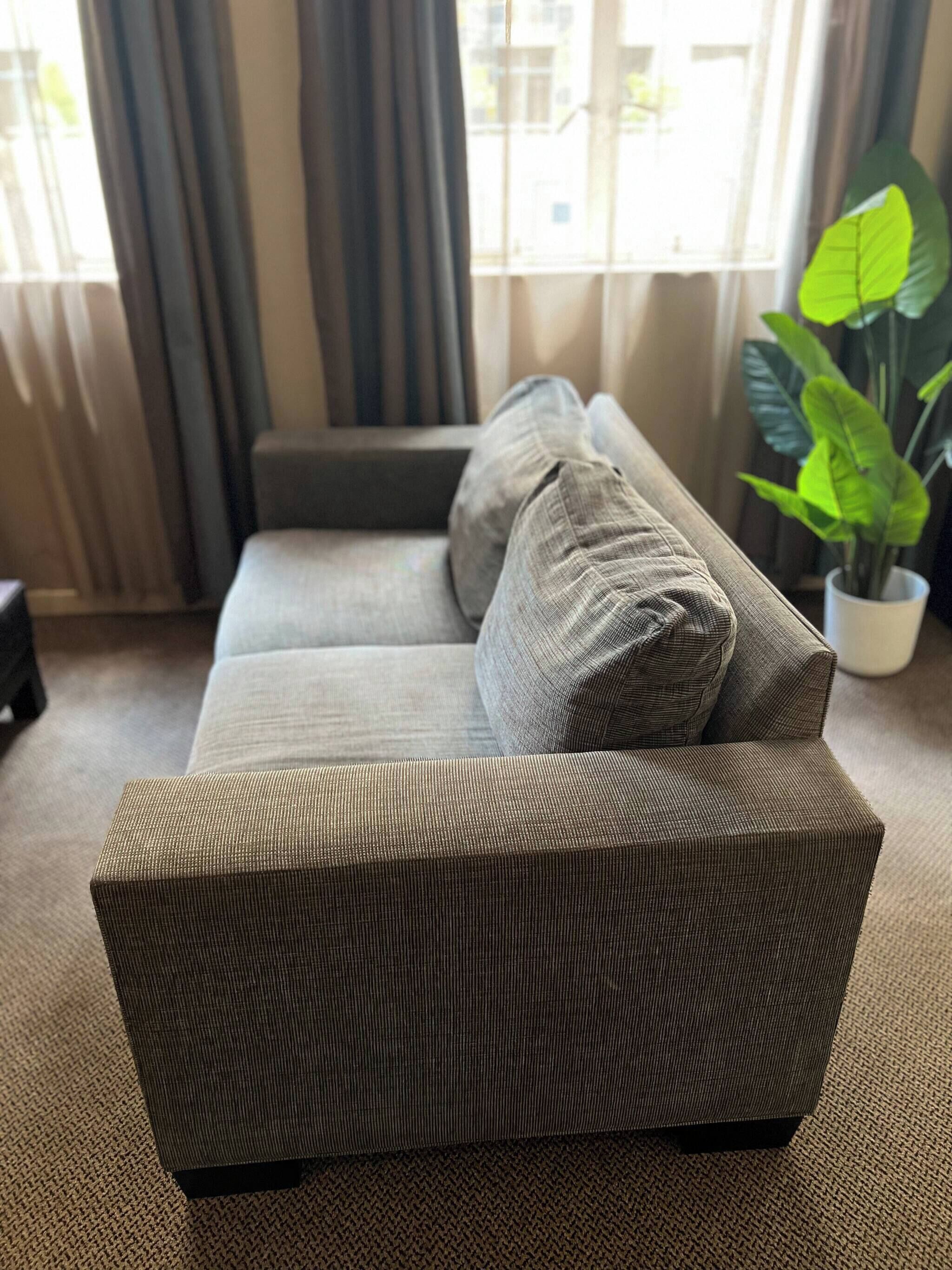 En stue med sofa, en potteplante og et vindue med gardiner.