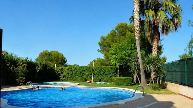 A swimming pool with a tiled deck, surrounded by greenery and palm trees. - Th46 Casa Adosada en Salou Para 6 Personas (Salou)