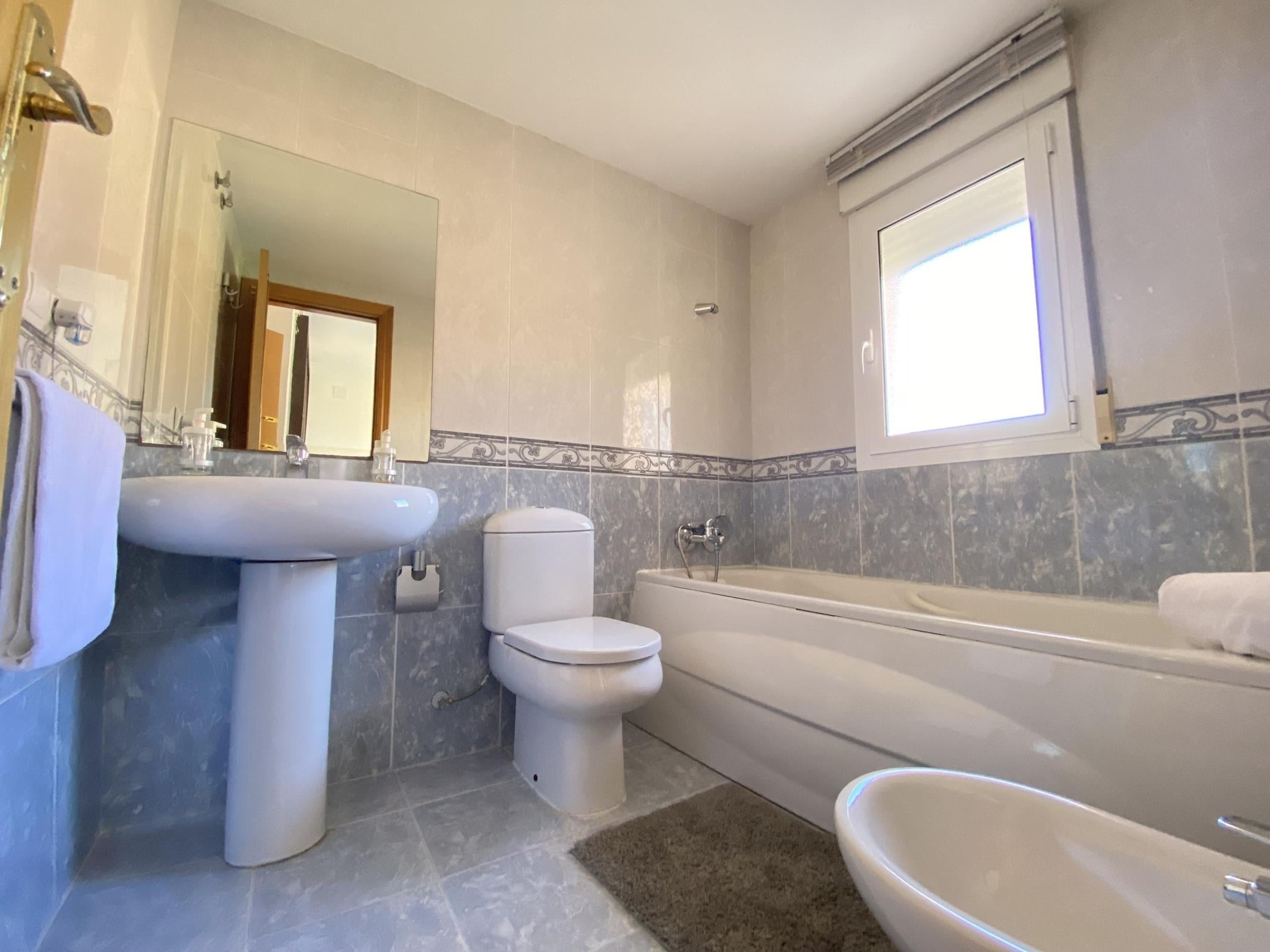 Et badeværelse med vask, toilet, badekar og et spejl.