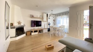 A living room with a fireplace, TV, and a dining area with chairs and a table. - Th46 Casa Adosada en Salou Para 6 Personas (Salou)