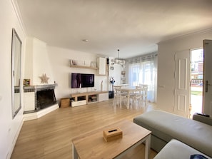 A living room with a fireplace, TV, and a dining area with chairs and a table. - Th46 Casa Adosada en Salou Para 6 Personas (Salou)