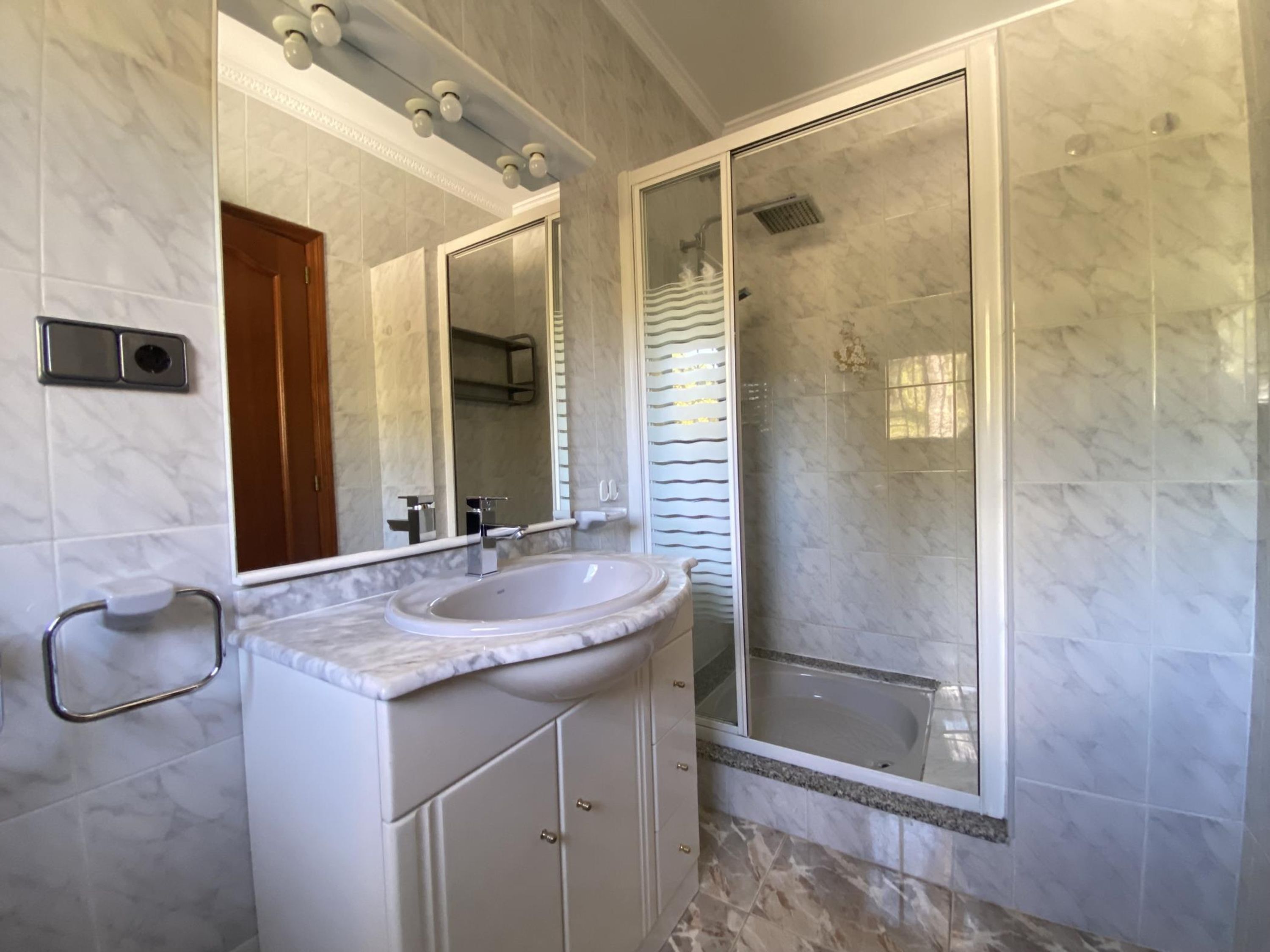 Een badkamer met een marmeren wastafel, een grote spiegel en een douche met glazen wanden.