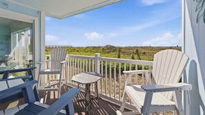 A balcony with Adirondack chairs and a table, overlooking a grassy landscape and a distant structure. - Oceanfront 3BD/2BA-First Floor-Beautifully Decorated-Family Friendly (North Myrtle Beach)